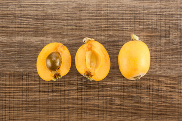 Fresh orange Japanese loquats collection top view isolated on brown wood background one cut in two halves with a seed and whole.