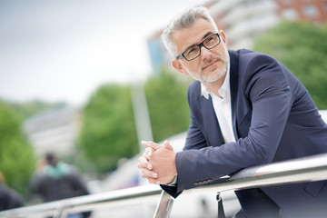 Businessman in city street leaning on bridge rail