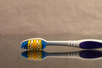 A toothbrush close-up, laid on its side on a reflective surface against a background of crumpled...