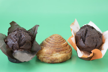 Two chocolate muffins and a cinnamon roll on a green background close-up