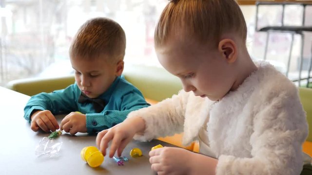 Cute kids in cafe, children sit at table and play the kinder surprise toys