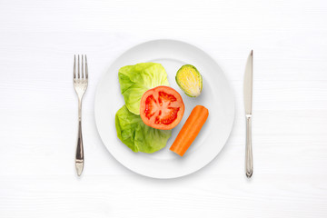 Diet meal with vegetables. In the plate are salad, tomato, cucumber and carrots. Next to the plate are a spoon and a fork. Flat view, white space.