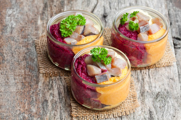 Herring  salad with colorful vegetables in a small glass jars on wooden table