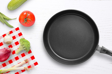 Empty pan on kitchen table with vegetables beside. Vegetarian cusine composition.