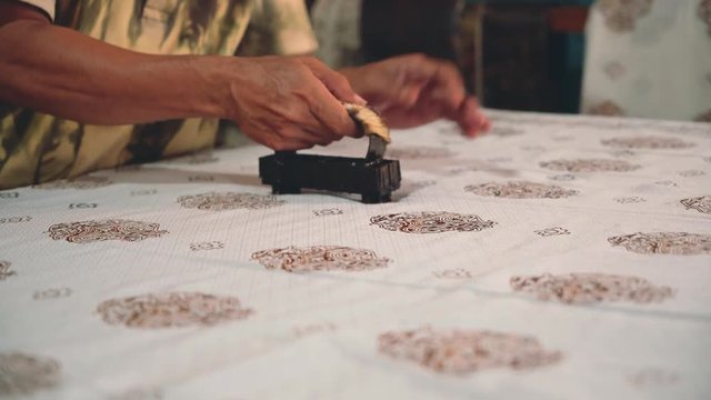 Close up of adult indonesian man hands applying hot wax pattern to fabric using cap to make batik