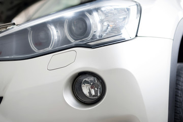 Obraz na płótnie Canvas The headlamp of the new clean white sports car is of aggressive form with a part of the bonnet and black wheel, bumper and partronik.