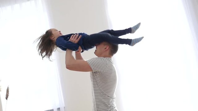 Happy family at home - father entertain little child daughter throw and spin her in air and then they falling on a bed
