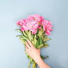 Female hand holding bouquet of pink peony flowers. Holiday background, top view.