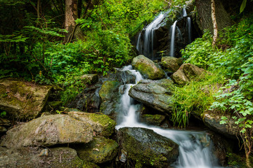 Cascade falls over mossy rocks in Czech forest