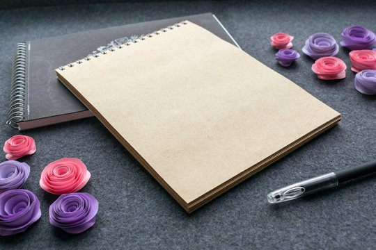 Mockup with empty sketchbook or notebook with brown kraft paper, black pen and paper pink and lilac roses on dark felt background. Cute mock up for elegant design to display your artworks.
