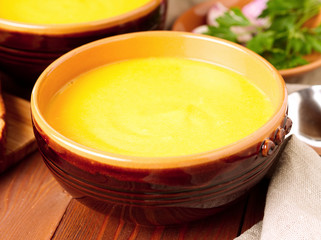 brown bowl of pumpkin soup on brown dark wooden background, side view.