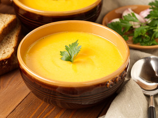 brown bowl of pumpkin soup with parsley on brown dark wooden background, side view, close up