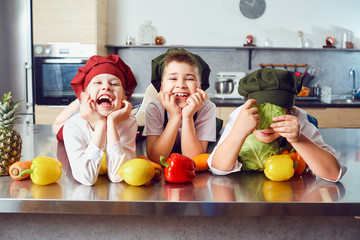 Funny children in the uniform of cooks on the table in vegetables in the kitchen.
