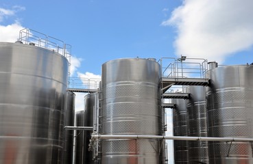 Large steel tanks for wine maturation, cloudy sky background, winery modern equipment, closeup, bottom view