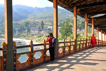 Fototapeta na wymiar Female tourist taking photograph at PUNA MOCCHU BAZAM : Antique wooden bridge at Punakha Dzong Monastery or Pungthang Dewachen Phodrang Bhutan