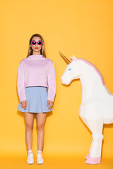 young stylish female model in sunglasses and decorative unicorn on yellow background