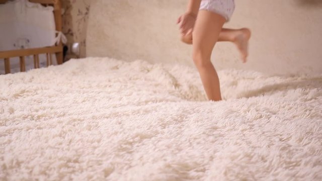 Little kid girl play at home have fun running on a bed legs in slow motion