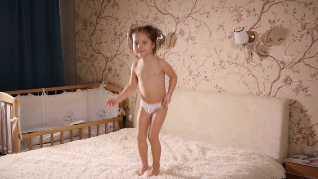 Little kid girl play at home have fun jumping on a bed falling on her back in slow motion