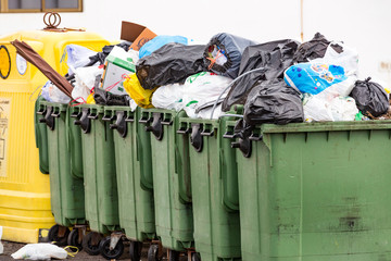 Many green over flowing garbage dumpsters in a row.