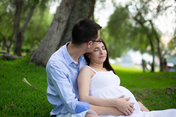 Pregnant couple walks in the park together holding hands