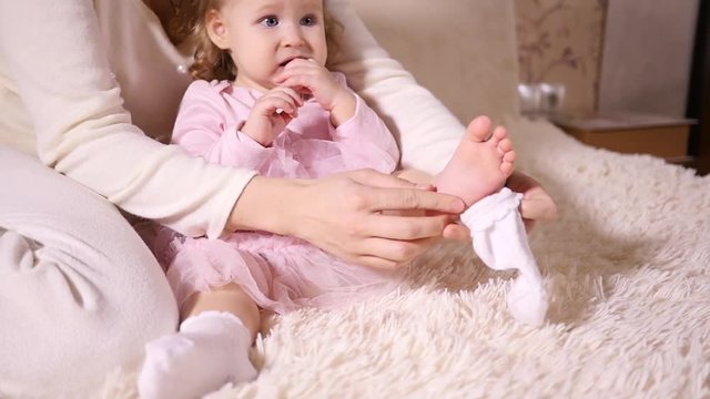 Maternal care, mother tenderly wears on a sock on a little foot of her baby girl daughter