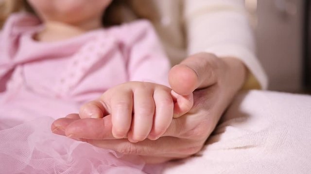 Mother hand holding strocking a little hand of her toddler baby girl daughter closeup
