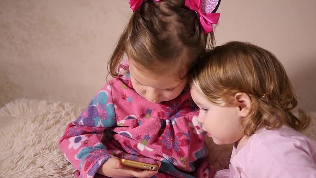 Little kids girlds sisters sit at home watching a smart phone cartoons - children portrait