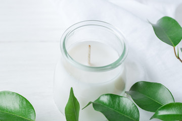 Obraz na płótnie Canvas White Candle in Glass Jar Fresh Tree Branches with Tender Green Leaves on Wood and Cotton Linen Fabric Background. Spa Wellness Body Care Meditation Purity Concept. Minimalist Style. Copy Space