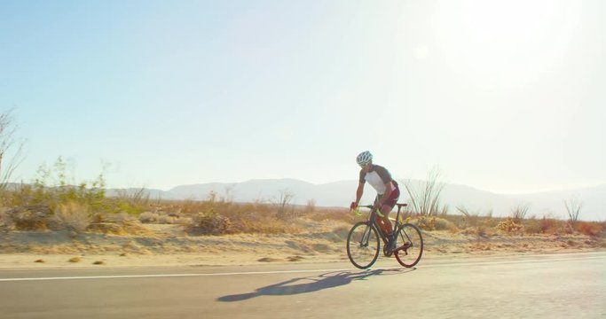 Slow motion young man cycling on road bike outside on desert road on sunny day 