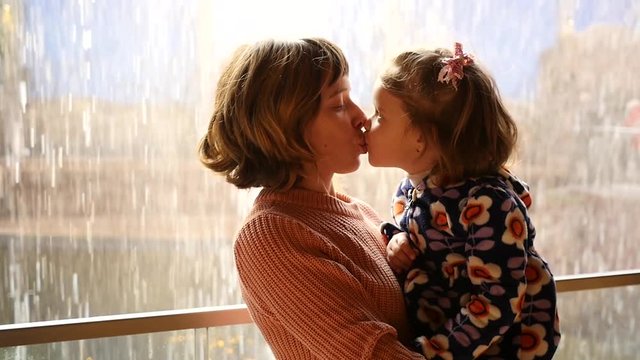 Mother holds a child girl happy enjoy water falling kissing in slow motion