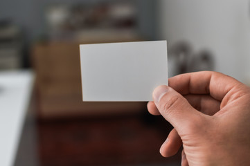 Closeup image of holding business card, person hand showing plain mock up space on professional office background. Businessman communication information