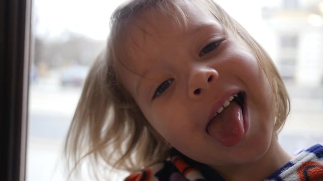 Cute grimace face portrait of a little child girl joyfully show tongue under air flow