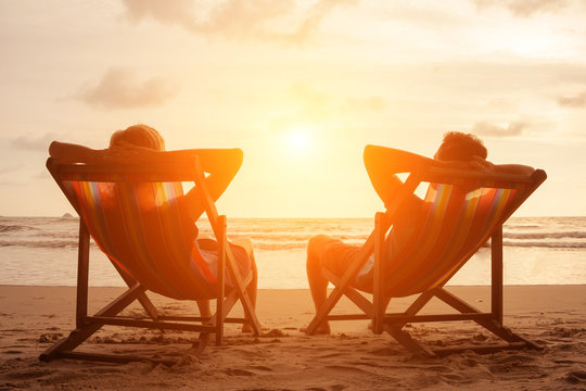 Romantic holiday travel. Silhouette of happy young couple sitting in deck chairs in luxury beach hotel at sunset near the sea. Love and relationship concept. Summer vacation in tropical paradise islan