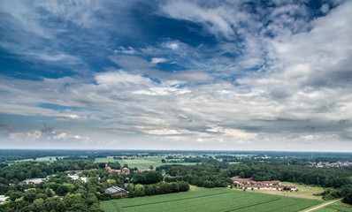 Fototapeta na wymiar Aerial view of an area of arable land at the edge of a village with connected forest areas and trees along a road in Germany, dramatic sky