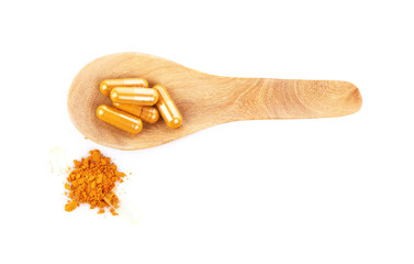 Turmeric capsules with wooden spoon isolated on white.