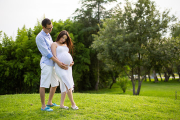 Pregnant couple walks in the park together holding hands