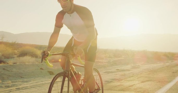 Slow motion young man cycling on road bike outside on desert road at sunset with lens flare 