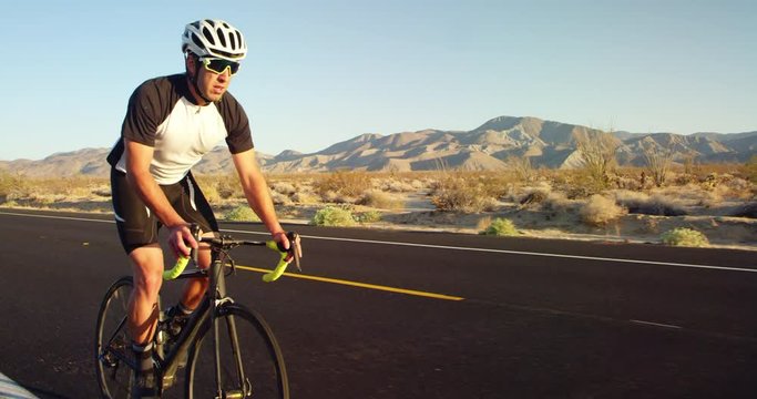 Slow motion young man cycling on road bike outside on desert road on sunny day 