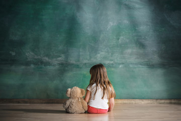Little girl with teddy bear sitting on floor in empty room. Autism concept