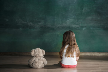 Little girl with teddy bear sitting on floor in empty room. Autism concept