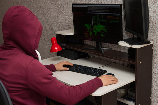 Hacker using the computer. Man in a red hoodie breaks the access to steal information and infects computers and systems