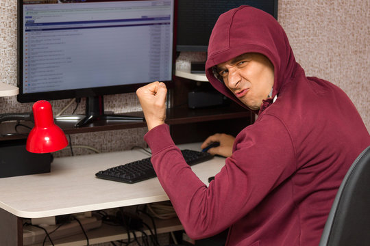 Internet troll with the evil face sitting at the computer. Very bad young man rejoices writing nasty things on the forum