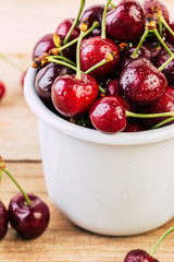 cherries in a white enamel mug on a wooden table, fresh cherry, seasonal berries, sweet cherry, ripe berries, berries in a mug