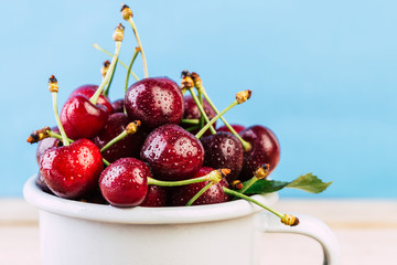 cherries in a white enamel mug on a wooden table, fresh cherry, seasonal berries, sweet cherry, ripe berries, berries in a mug