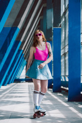 beautiful stylish girl in pink sunglasses and denim skirt roller skating and looking at camera