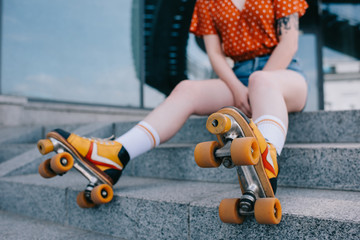 cropped shot of stylish young woman in roller skates sitting on stairs