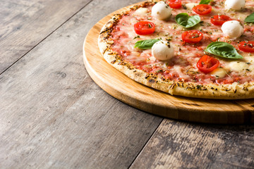 Pizza with tomatoes, cheese and basil on wooden table. Copyspace