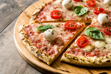 Pizza with tomatoes, cheese and basil on wooden table