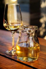 Bottle of white wine and glass on wooden table top. Glass of chilled white wine on table near the beach, in a restaurant tavern.