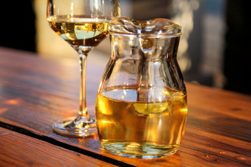 Bottle of white wine and glass on wooden table top. Glass of chilled white wine on table near the beach, in a restaurant tavern.